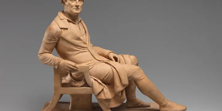 A terracotta statue of a gentleman reclining on a chair.