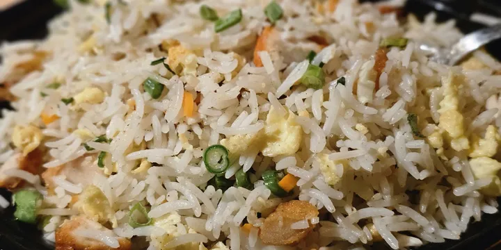A close-up of a serving of chicken fried rice, featuring fluffy white rice mixed with diced carrots, scrambled eggs, and pieces of chicken, garnished with chopped green onions. The dish is presented in a black bowl, with a slightly blurred background emphasizing the texture and ingredients of the fried rice. It was captured in Kozhikode, Kerala.
