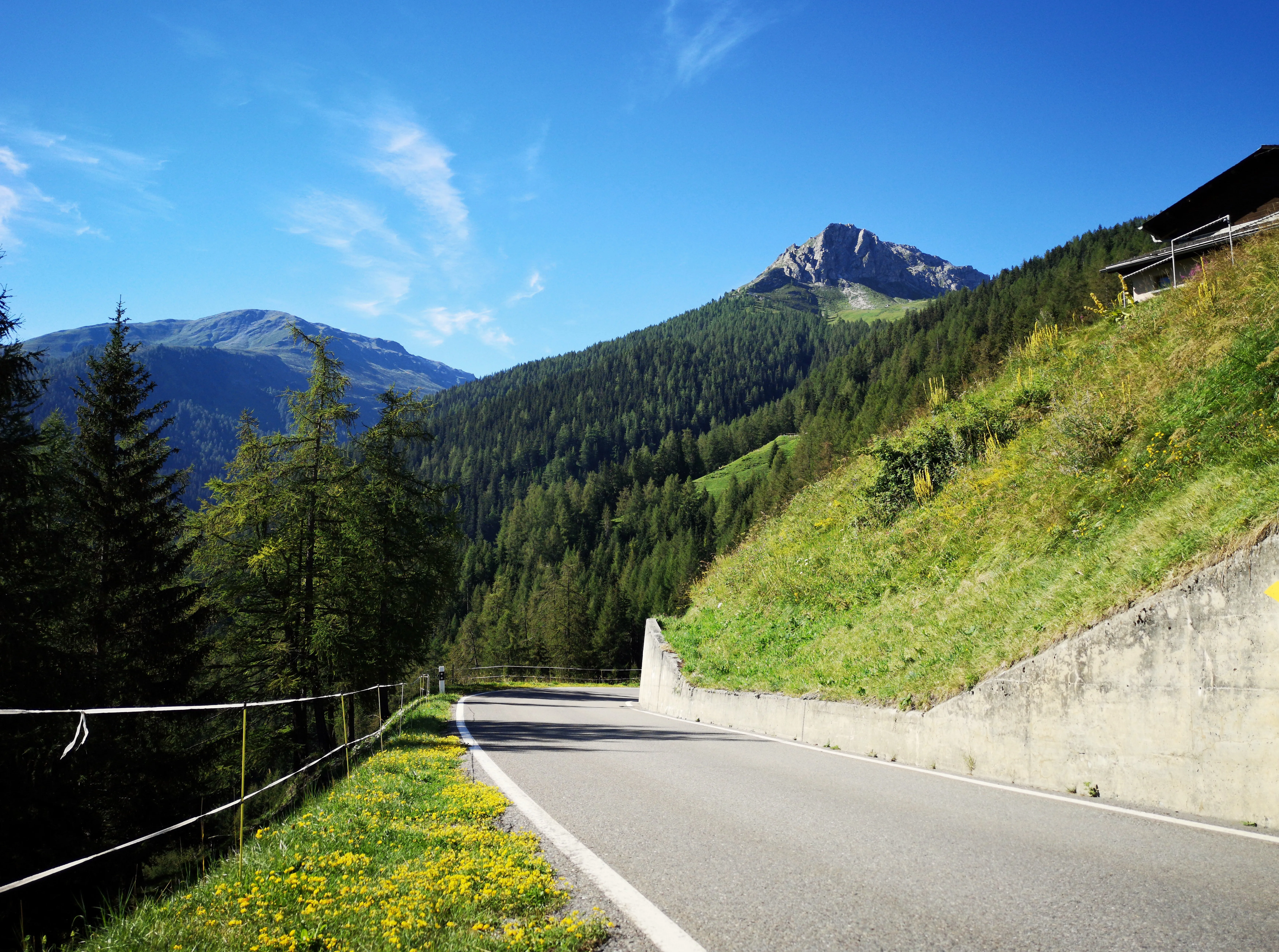 A photo of a curve in a mountain road. There is a ribbon marker along the left side before a steep drop-off. A concrete retaining wall is on the right side.