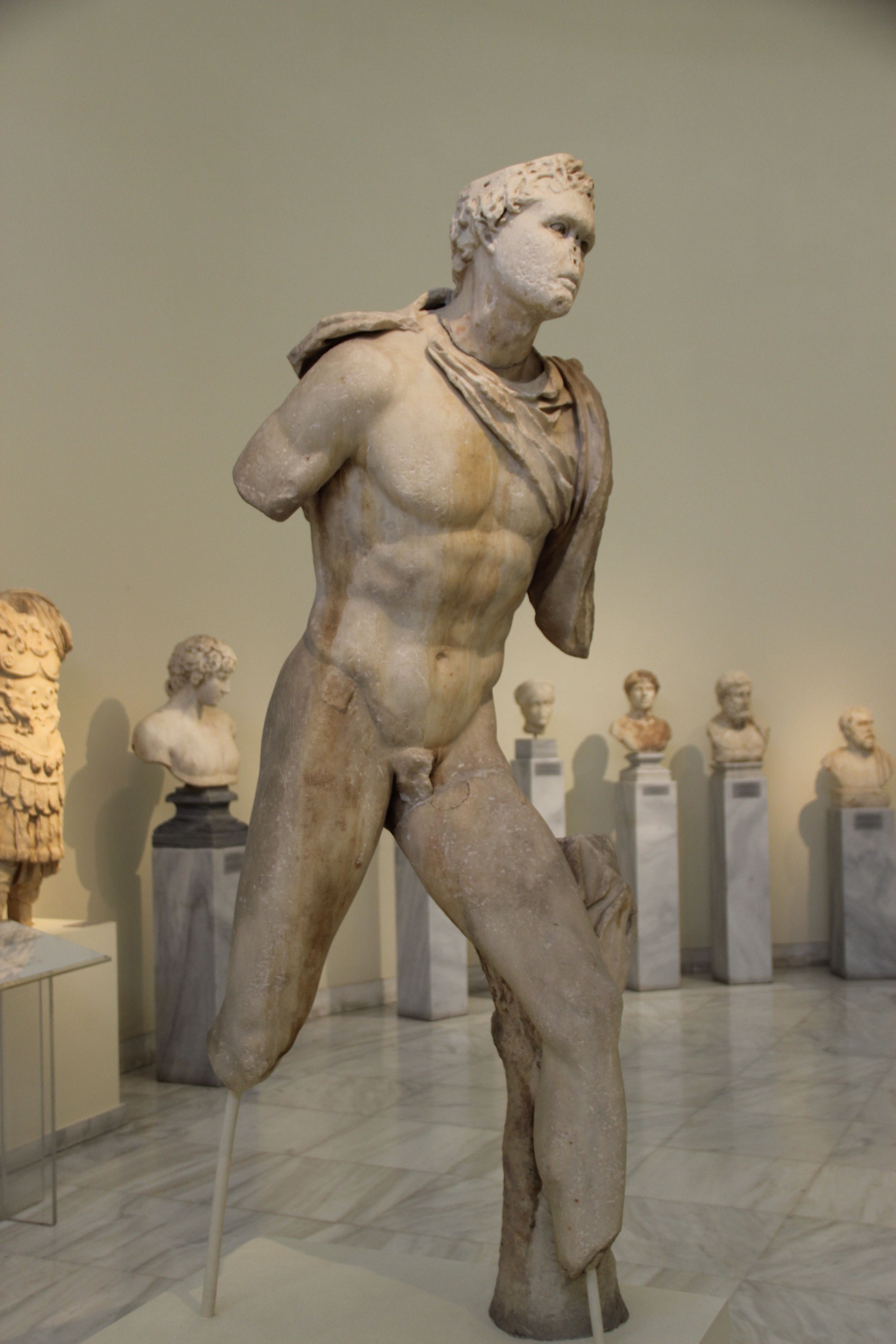A photo of a worn Greek marble statue of a male figure. The figure looks to be in motion, though its arms and feet are missing. Most of its face is worn away. The muscles are still well-defined.